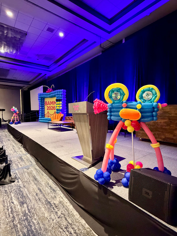 Movie camera balloon sculpture beside a conference stage backdrop.