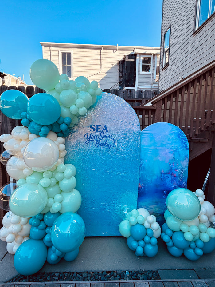 Ocean-themed baby shower backdrop with turquoise, mint and white balloons and Sea You Soon Baby lettering